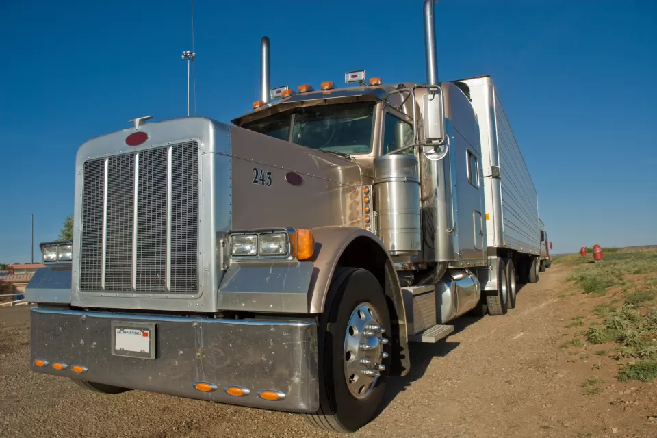 Front view of a tan semi-truck cab parked on a vacant piece of land with a clear blue sky in the background.